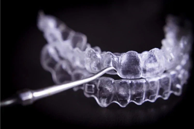 An image of clear aligners next to an instrument for oral cleaning