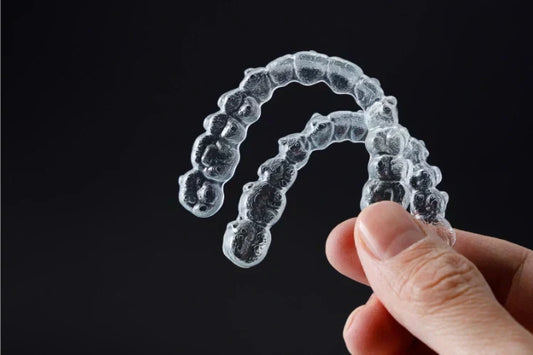 A hand holding clear retainers for upper and lower teeth
