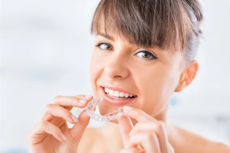 A woman holding clear aligners and smiling