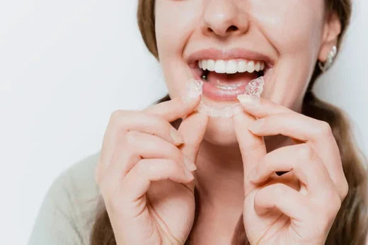 A woman holding clear aligners while looking in the mirror