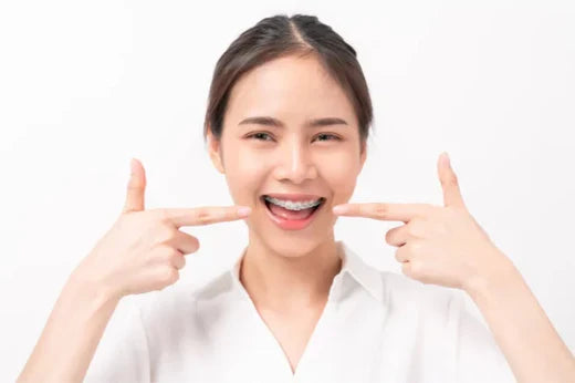 A woman with braces smiling and pointing at her teeth