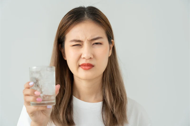 Woman wincing from tooth sensitivity while holding a glass of water