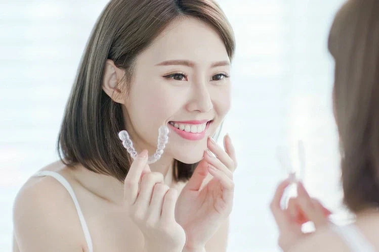 A woman applying clear retainers while looking in the mirror.