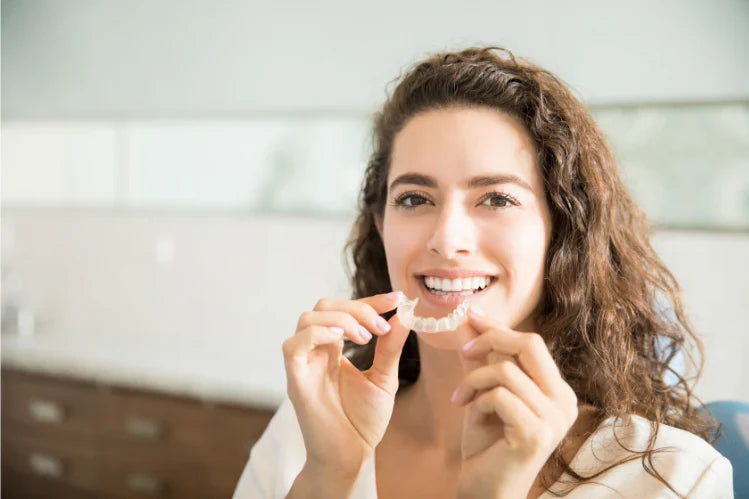A woman smiling while putting on her clear retainer