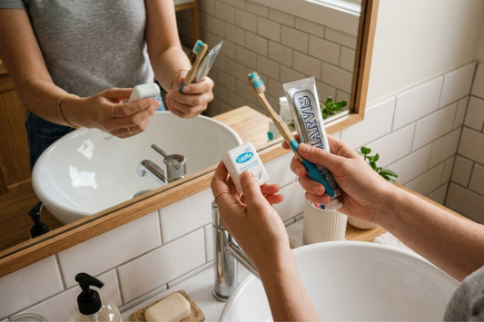 Hands holding dental floss and a toothbrush at a bathroom sink