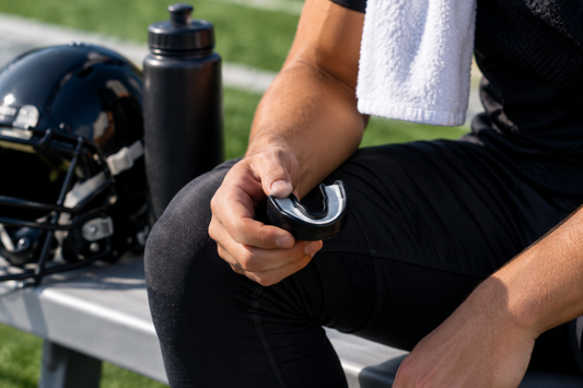 Athlete holding a black mouth guard on a bench beside a helmet