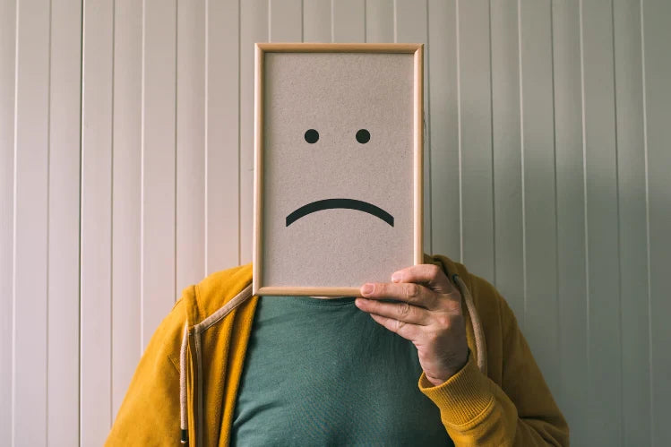 A man holding a sad face frame over his face