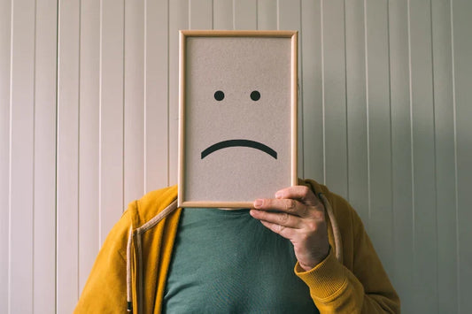 A man holding a sad face frame over his face