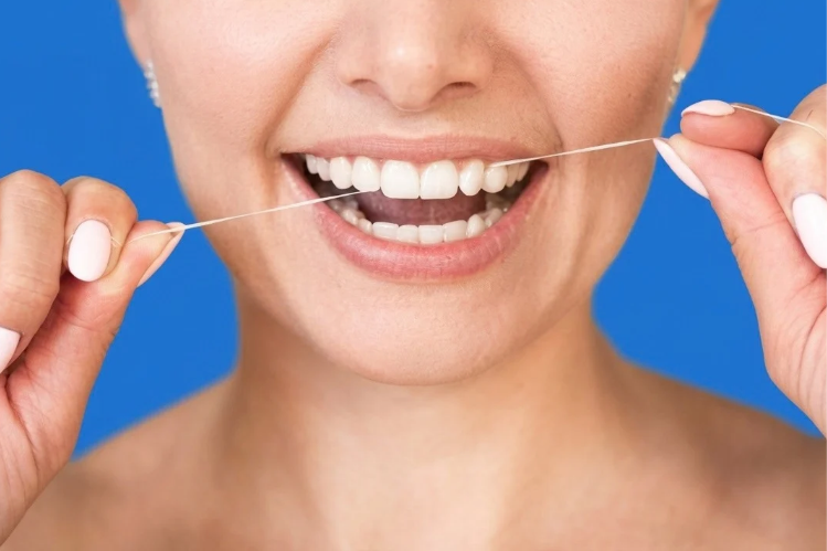 Smiling woman flossing her teeth with dental floss