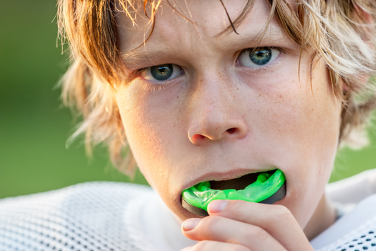 Young boy putting a green sports mouth guard in his mouth