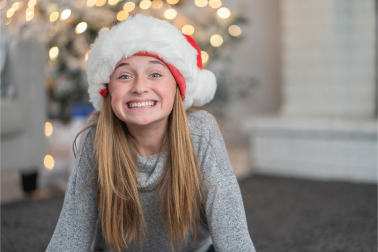 Smiling girl in a Santa hat in front of a Christmas tree