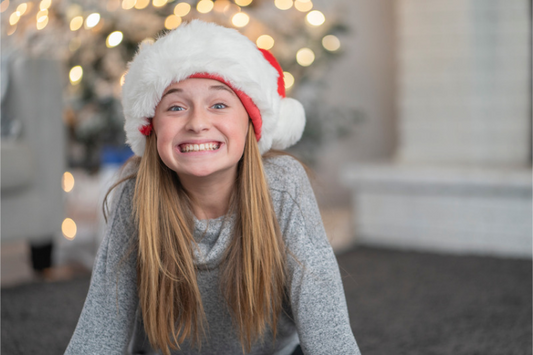 Smiling girl in a Santa hat in front of a Christmas tree