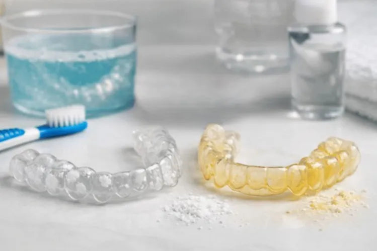 A clean, clear aligner and a yellow clear aligner with a tooth brush on the side and a water glass in the background 