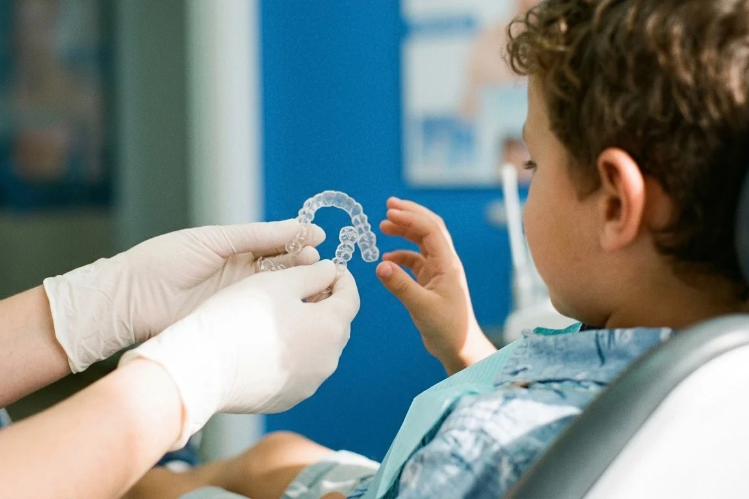 Dentist holding a clear aligner near a young boy in a dental chair