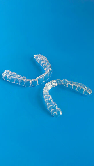 Two clear dental aligners placed on a blue background for orthodontic use.